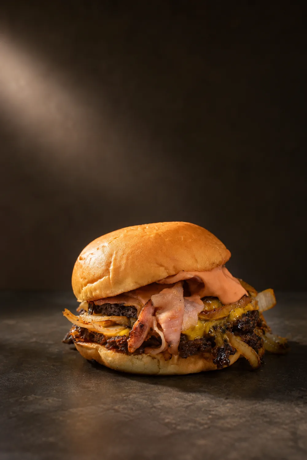 Hamburguesa con cheddar, panceta y cebolla caramelizada sobre fondo oscuro